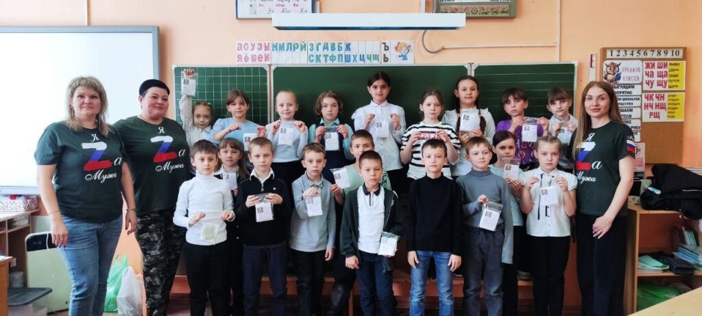 Ребята совместно  с волонтерами стоят у доски с пакетиками сухого душа