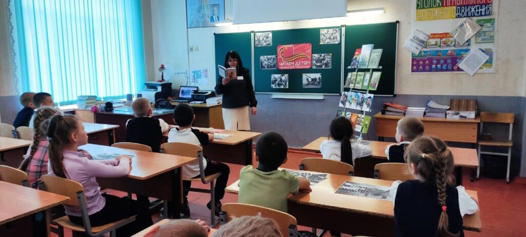 Ребята сидят за патами и слушают, как учитель читаем им произведения о Великой Отечественной войне