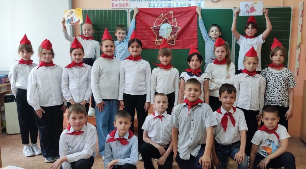 Ребята одеты в галстучки и пилотки, держат флаг пионерии